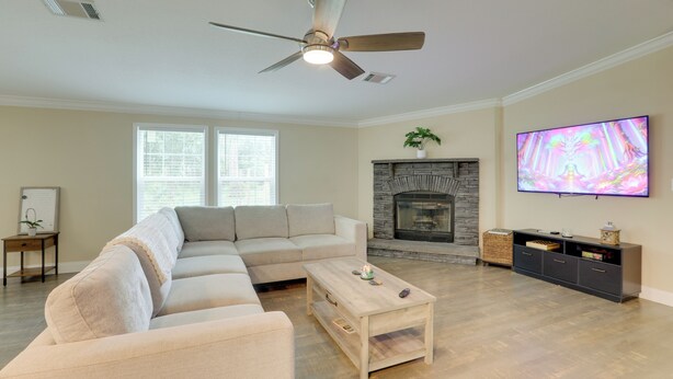 A living room with a sectional sofa, a coffee table, a fireplace, a television, and a ceiling fan.
