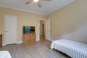 Un dormitorio con una cama, un televisor sobre un mueble de madera y un ventilador de techo.