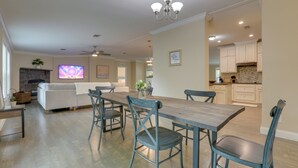A spacious dining area with a long table and chairs, a kitchen with white cabinets, and a living area with a sofa and TV.