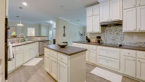 A kitchen with white cabinets, a central island, a backsplash with mosaic tiles, and a hanging light fixture.