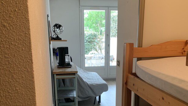 Une petite pièce avec un lit superposé, un bureau doté d’une machine à café et une fenêtre donnant sur un paysage verdoyant.