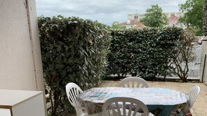 Une terrasse avec une table et des chaises, un meuble blanc et une vue sur un bâtiment et des arbres en arrière-plan.