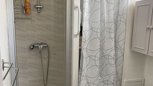 Une salle de bain avec une douche à l’italienne, des toilettes et un rideau de douche orné d’un motif géométrique.