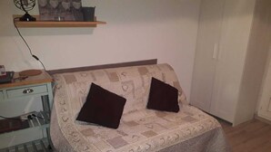 Une petite pièce agréable, dotée d’un canapé-lit, d’une étagère en bois au-dessus et d’un petit bureau avec une chaise.