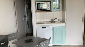 Une cuisine compacte équipée d’un four à micro-ondes, d’un lave-vaisselle et d’un évier. On y trouve une table avec une chaise et un petit meuble de rangement.