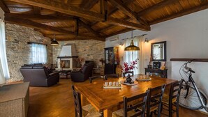 Un interior rústico con pared de piedra, techo de madera, chimenea, una mesa de comedor con sillas y una bicicleta.