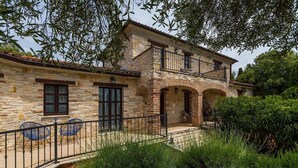 Una casa de piedra con balcón, patio cercado y mobiliario exterior.