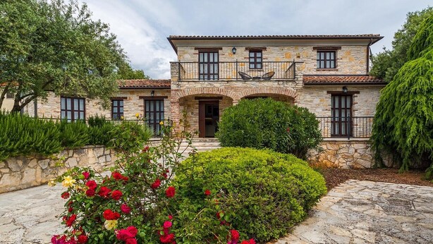 Un edificio de piedra con balcón, rodeado de setos cuidados y plantas con flores.