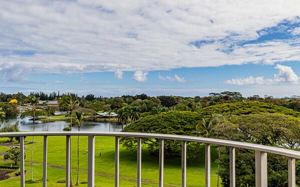A scenic view from a balcony overlooking a lake, lush greenery, and distant trees.
