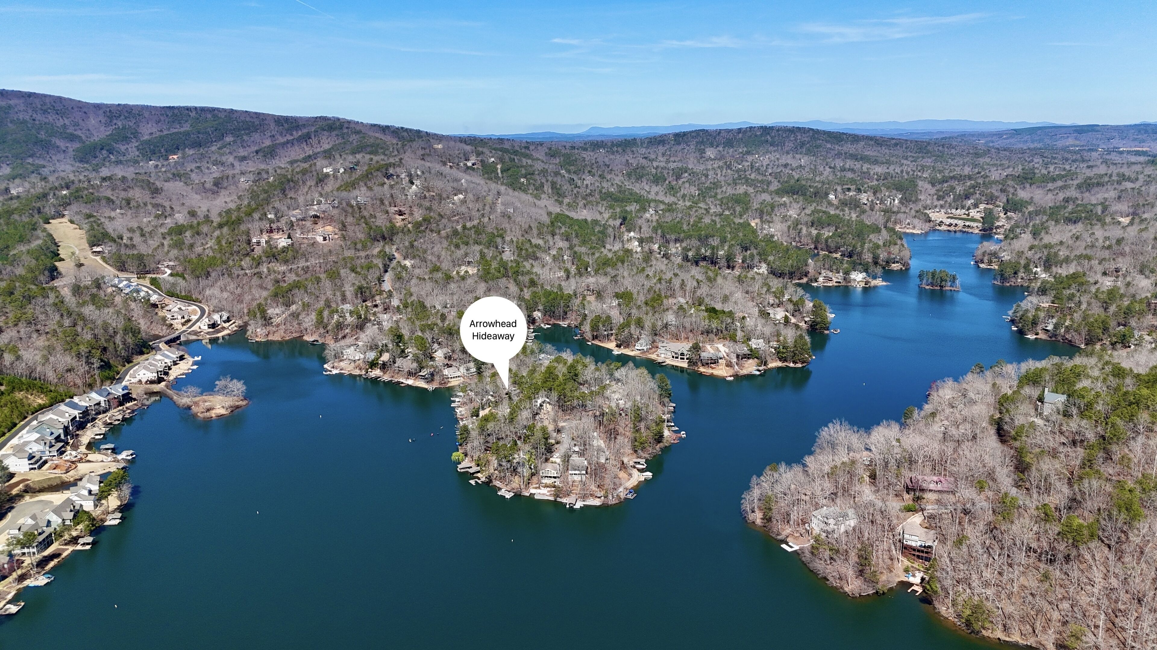 Vue aérienne d’Arrowhead Hideaway, avec un lac entouré de collines boisées, des quais pour bateaux et une route sinueuse.