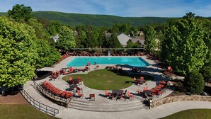 Ein Pool mit einer umlaufenden Terrasse, Sitzbereichen und Blick auf eine hügelige Landschaft.