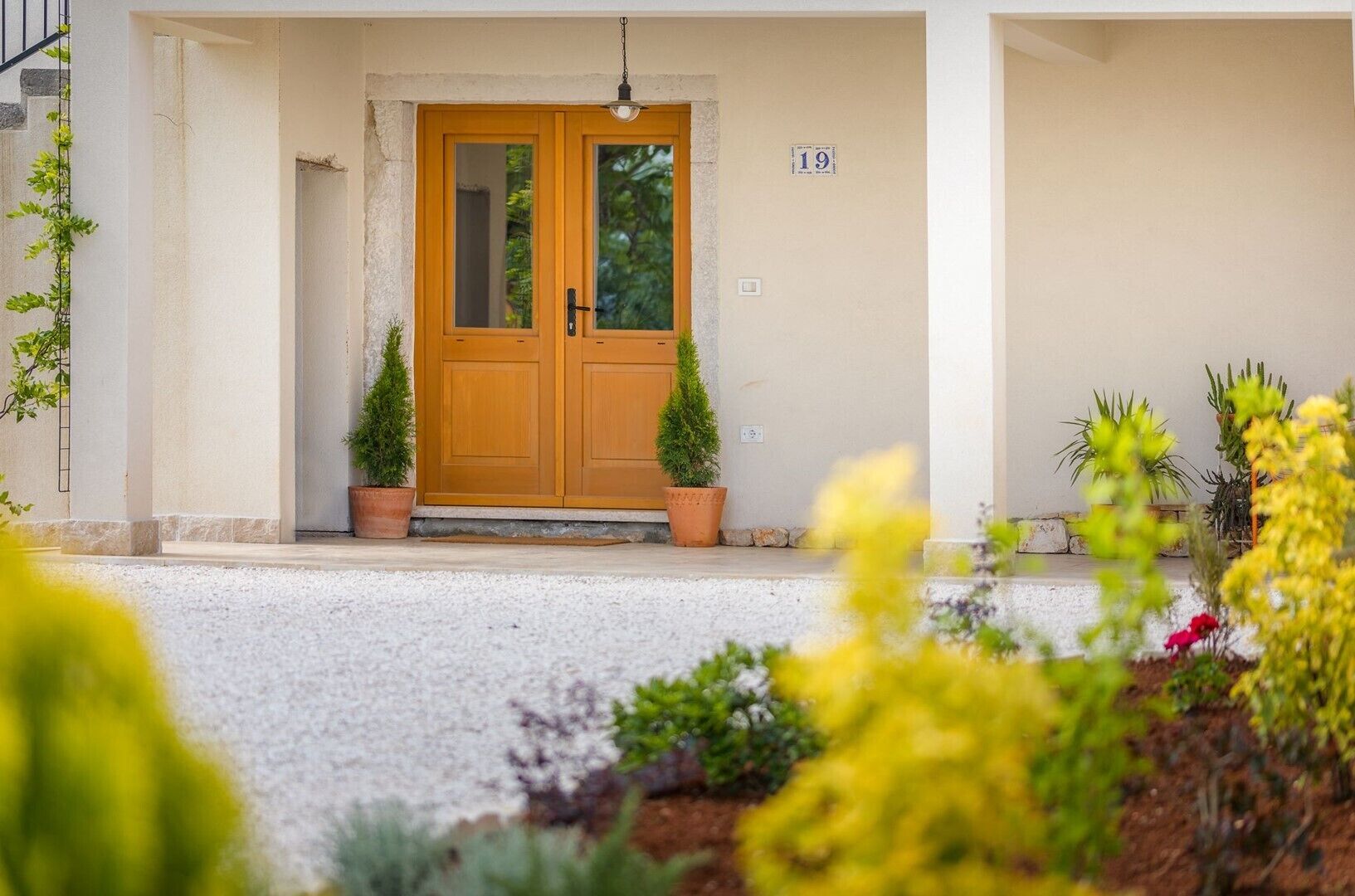 A building entrance with a double wooden door, numbered 19, and potted plants on either side.