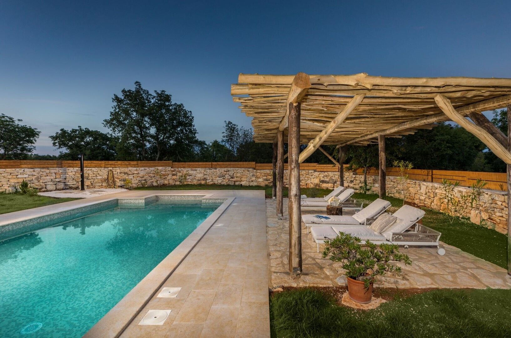 A swimming pool with a wooden pergola and lounge chairs.