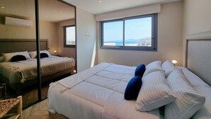 Habitació d'hotel moderna amb un llit gran, un altre més petit, una finestra amb vista al mar i un armari amb mirall.