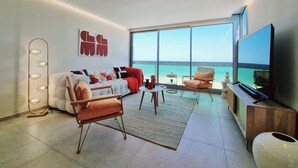 Un saló modern amb un gran finestral amb vista al mar, un sofà, una taula de centre i una televisió.