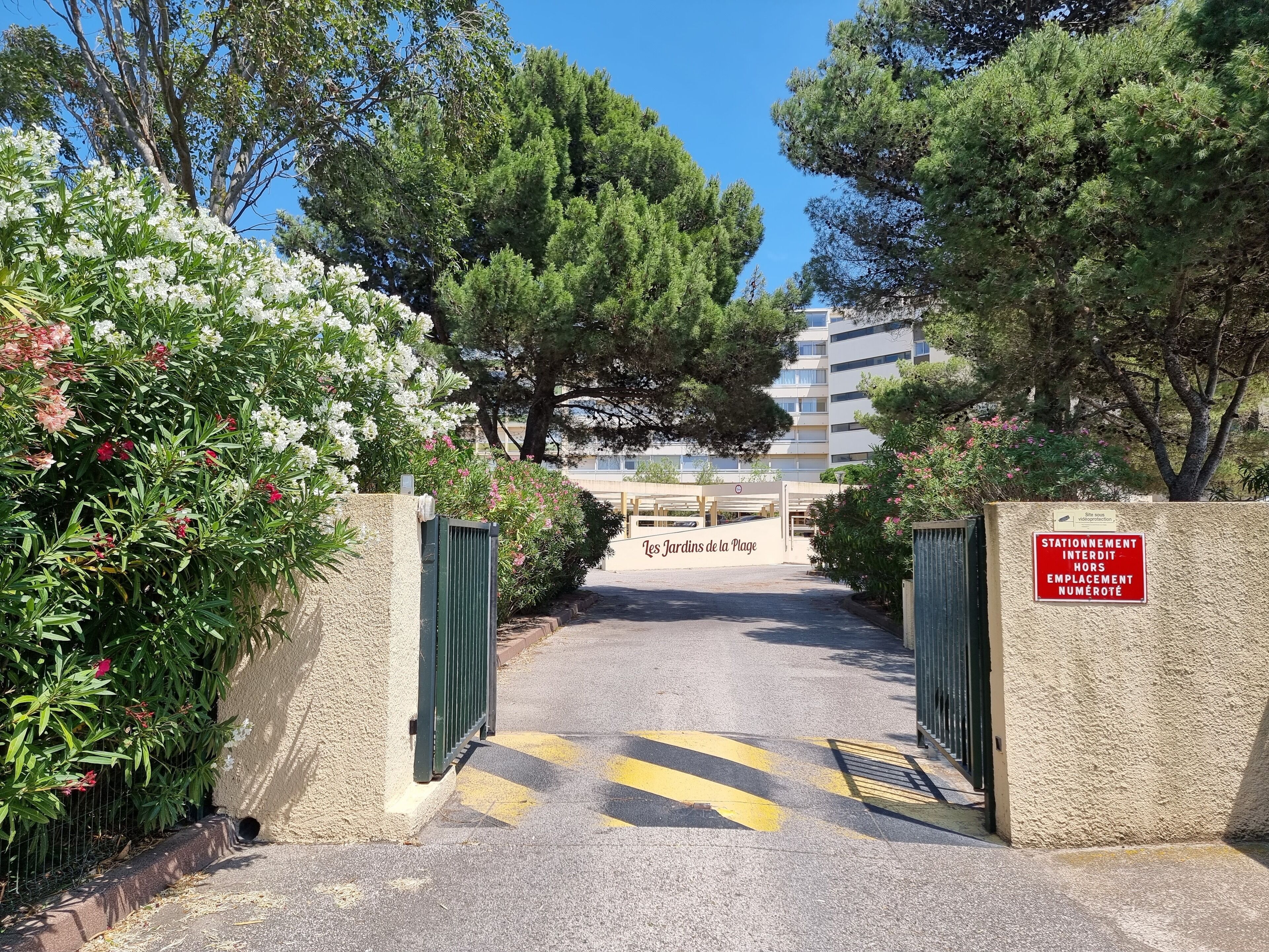 Une entrée fermée par un portail donnant accès à un immeuble, avec un panneau indiquant un espace de stationnement.