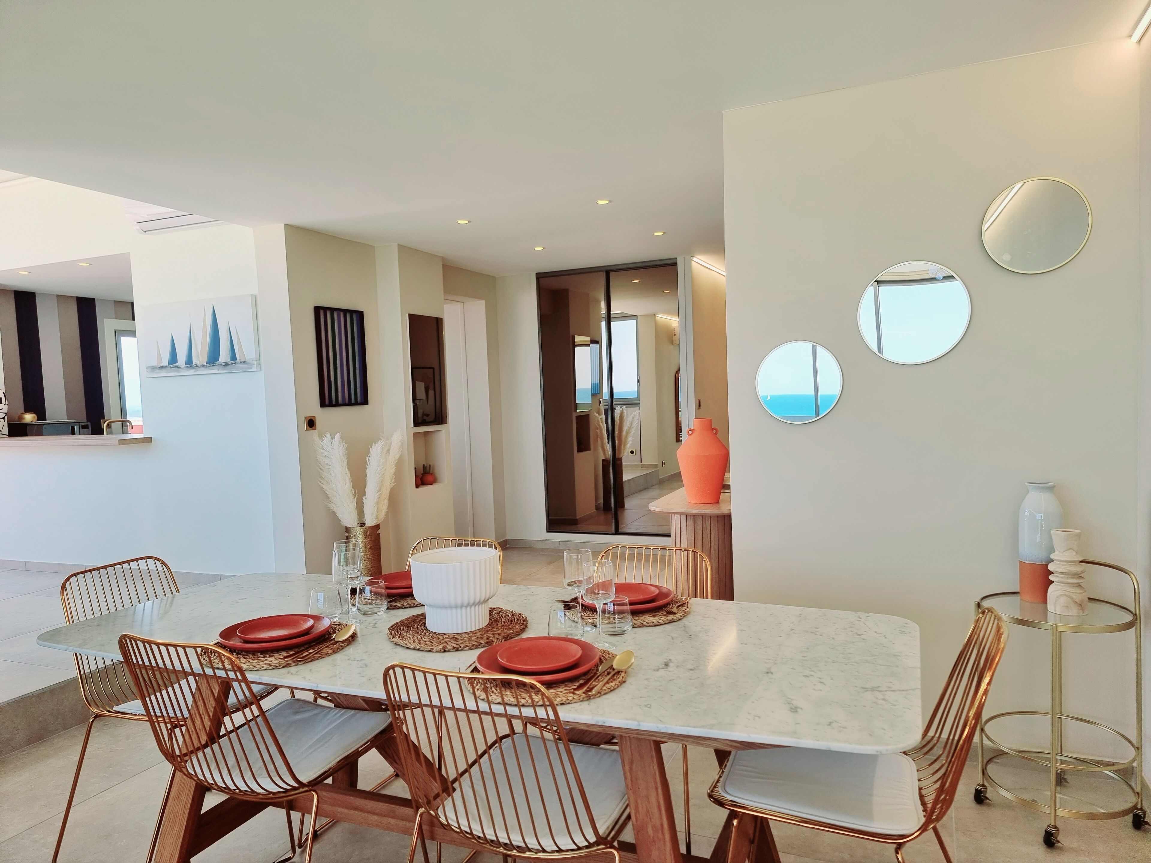Una zona de menjador moderna amb taula de marbre, plats vermells i blancs, i cadires de coure.