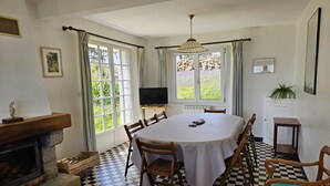 Comedor con piso a cuadros, chimenea, televisor y vista al jardín a través de las ventanas.