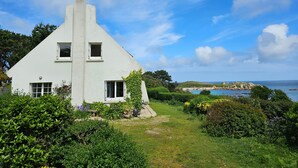 Una casa blanca con techo empinado, rodeada de exuberante vegetación y vistas al mar.