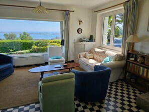 A living room with a view of the sea, a sofa, a chair, a coffee table, and a bookshelf. - Maison de Vacances à Louer sur L'ile Callot - Ker Douara (Carantec)