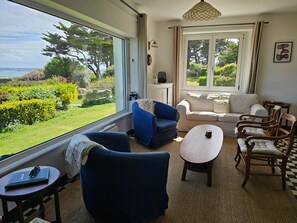 A room with a view of the sea, a sofa, a blue armchair, a wooden chair, and a small table with a laptop and glasses. - Maison de Vacances à Louer sur L'ile Callot - Ker Douara (Carantec)