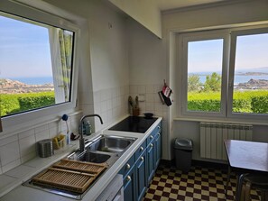 A kitchen with a view of the sea, checkered floor, and a window with a view of greenery. - Maison de Vacances à Louer sur L'ile Callot - Ker Douara (Carantec)