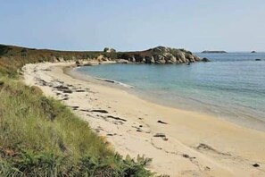 Una playa con arena, agua cristalina y afloramientos rocosos a lo lejos.