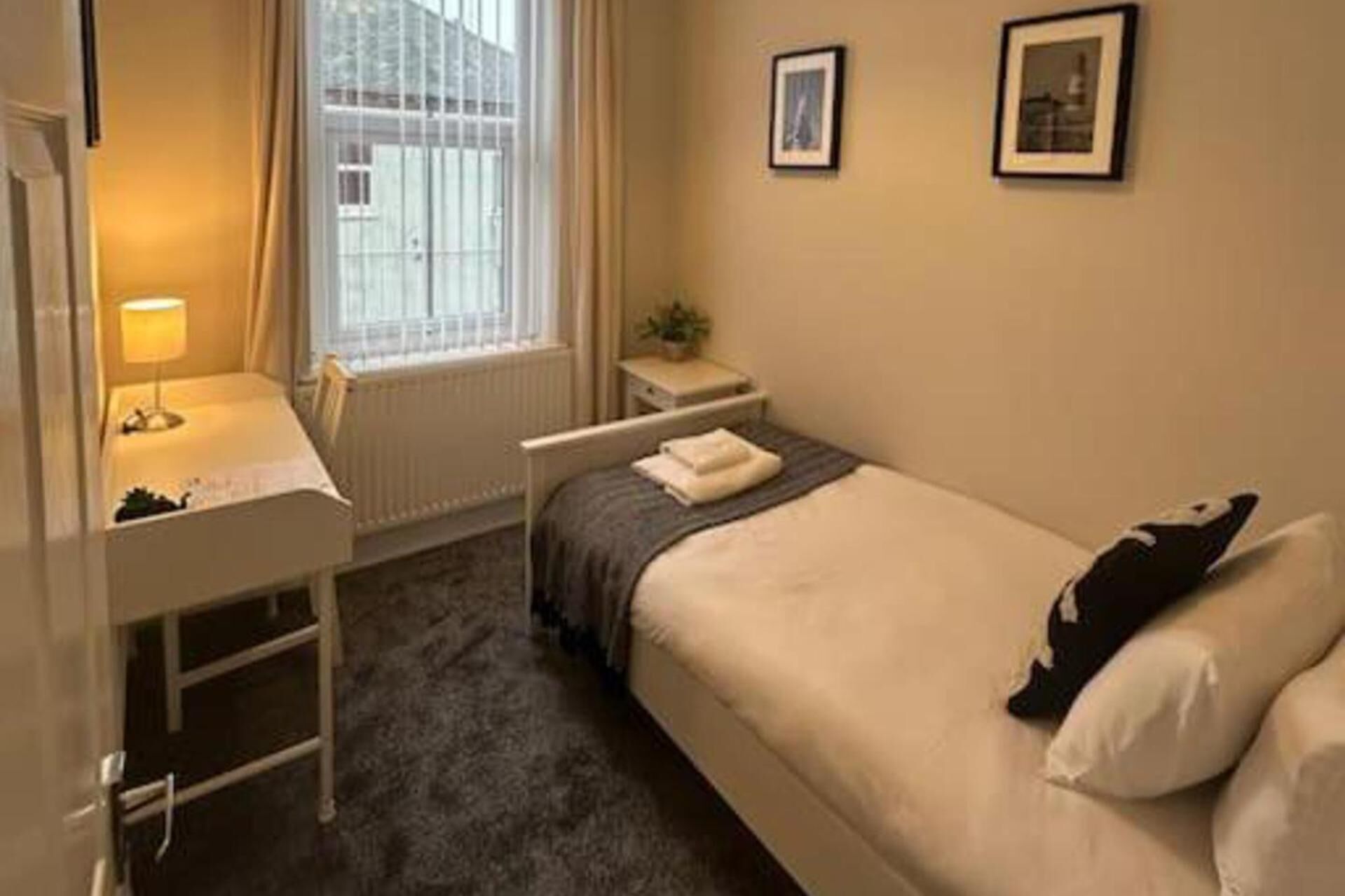 Une petite chambre à coucher, bien rangée, avec un lit simple, une table de chevet, une chaise, un bureau et une fenêtre avec des rideaux.