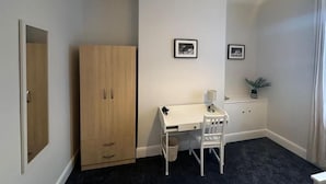 Une pièce comprenant une armoire en bois, un bureau blanc avec une chaise, et deux tableaux encadrés accrochés au mur.