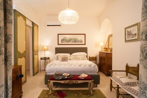 A bedroom with a bed, bedside table, lamp, dresser, chair, and artwork on the wall.