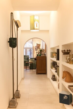 A hallway with a lamp, a hanging bag, a sofa, and a bookshelf with decorative items.