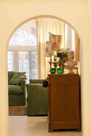 A room with a green sofa, a wooden cabinet with a bust, and a window with curtains.