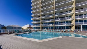 Une grande piscine extérieure avec plusieurs niveaux de balcons, entourée de chaises longues et d’une terrasse en bois.