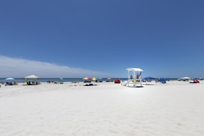 A beach with umbrellas, a lifeguard tower, and beach chairs. - Sanibel 606 (Gulf Shores)