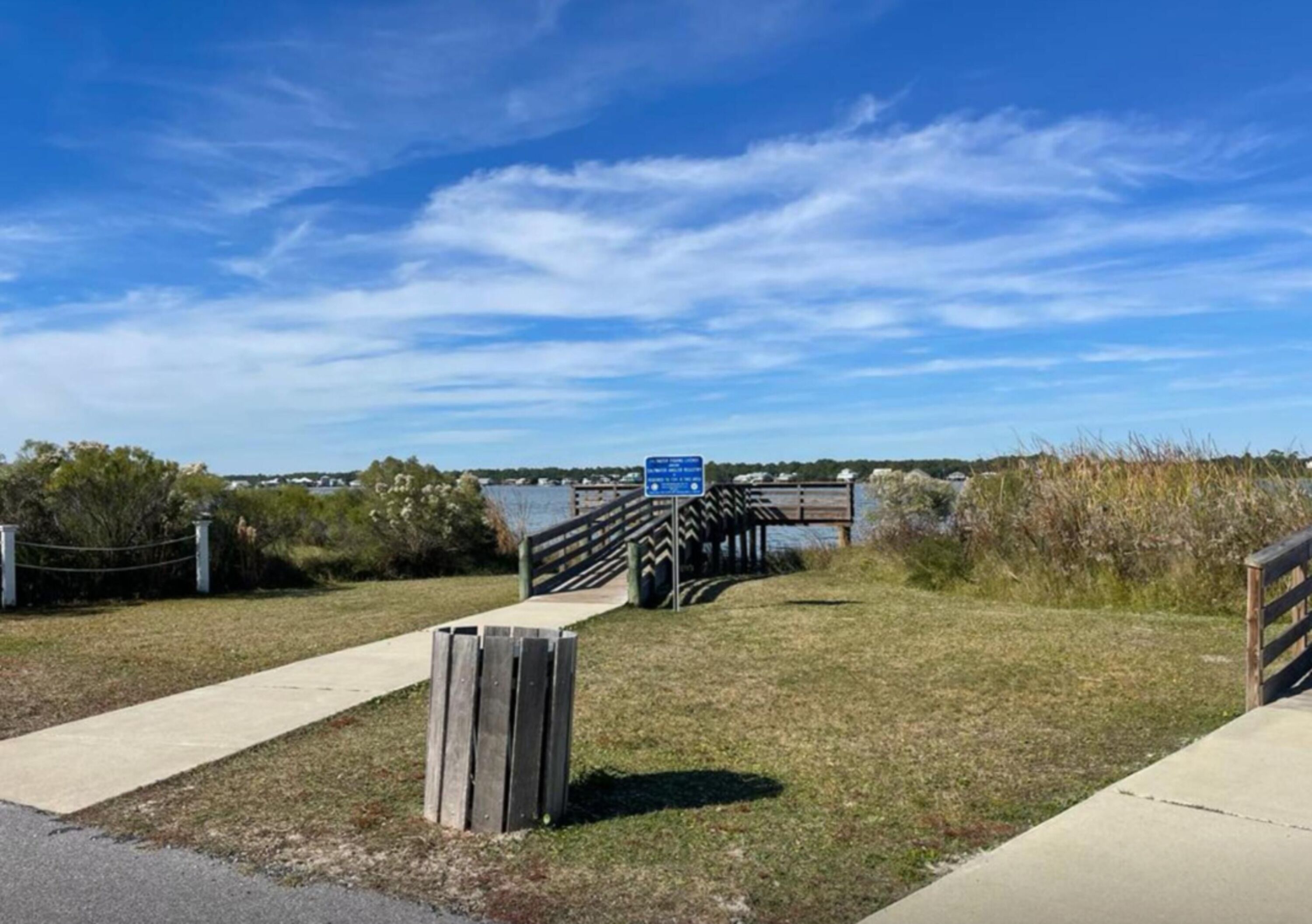 A pathway leading to a bridge over water, with a signboard and a wooden fence.