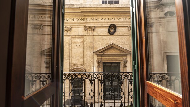 A view through a window with ornate iron railings, a stone building with classical architecture, and a plaque with inscriptions. - Via Giulia Charming Apartment with Balcony (Roma)