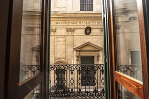 Blick durch ein Fenster mit aufwendiger Eisenverzierungen, ein Steinhaus im klassischen Stil und eine Tafel mit Inschriften.