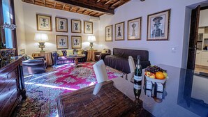 A room with a wooden ceiling, a red patterned carpet, a bed, a dining table with fruit, and framed pictures on the wall. - Via Giulia Charming Apartment with Balcony (Roma)