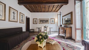 A living room with a dark sofa, a wooden coffee table with a vase of flowers, a dining area with a table and chairs, and a large mirror on the wall. - Via Giulia Charming Apartment with Balcony (Roma)