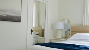 A neatly arranged bedroom with a bed, bedside table, lamp, and a mirror. - Welcome to Blue and Gold Getaway! (Morgantown)