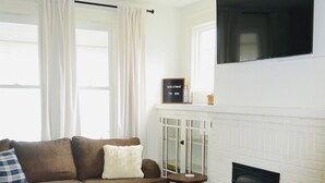 A living room with a brown sofa, a coffee table, a fireplace, and a ceiling fan. - Welcome to Blue and Gold Getaway! (Morgantown)
