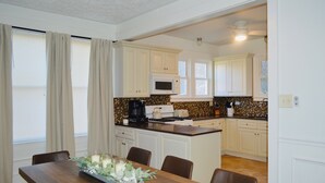 A modern kitchen with white cabinets, a microwave, and a coffee maker. There is a dining area with a wooden table and chairs. - Welcome to Blue and Gold Getaway! (Morgantown)