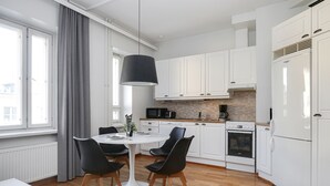 Eine moderne Küche mit weißen Schränken, einem Esstisch mit Stühlen, einer schwarzen Pendelleuchte und Blick auf die Stadt durch große Fenster.