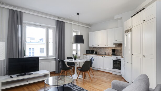 Ein modernes Wohnzimmer mit Flachbildfernseher, Glastisch und grauem Sofa.