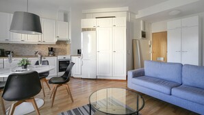 Eine moderne Küche mit weißen Schränken, einem Esstisch mit Stühlen, einem blauen Sofa und einem Glastisch.