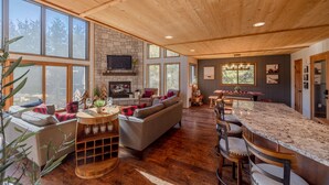 A spacious living area with a stone fireplace, large windows, and a wooden ceiling. - White Tail Lodge by Innsbrook Vacations! (Innsbrook)