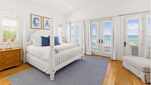 Een ruime slaapkamer met een groot bed, een houten dressoir en uitzicht op de oceaan door middel van schuifdeuren.