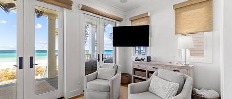 A living room with a beach view, a flat-screen TV, and a wooden cabinet.