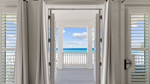 Uitzicht door een deuropening op een balkon, met een helderblauwe lucht en de oceaan op de achtergrond.