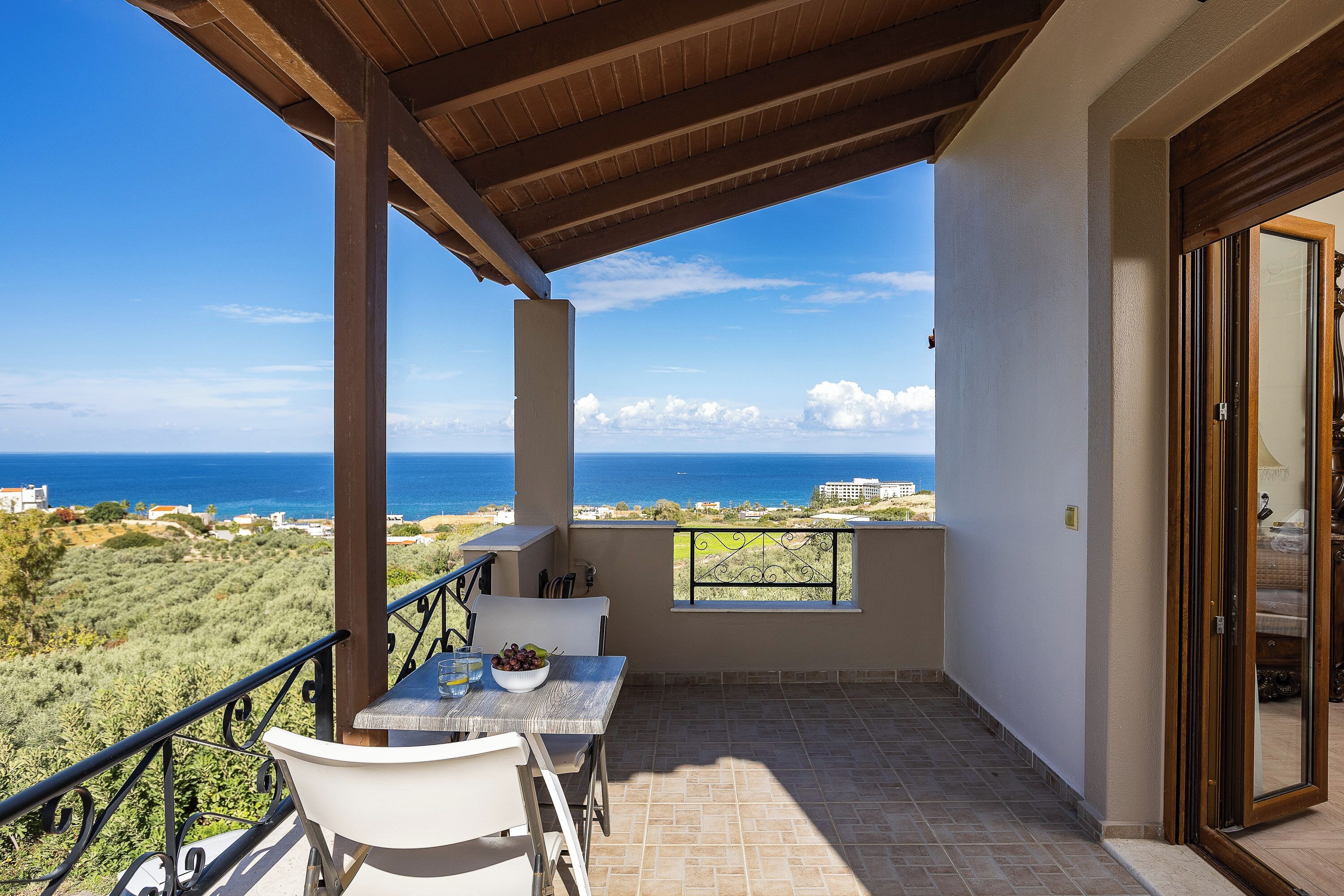 Ein Balkon mit Tisch und Stühlen, Blick auf das Meer und ein Gebäude im Hintergrund.